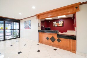 Un mostrador de recepción con encimera de madera y tablero negro, una pared roja con obras de arte y un suelo de baldosas.