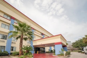 Ein mehrstöckiges Hotel mit roter und beiger Fassade, einem überdachten Eingang und Palmen im Vordergrund.
