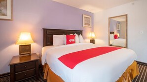 A hotel room with a large bed, two bedside lamps, a nightstand with a drawer, a mirror, and a framed picture on the wall.