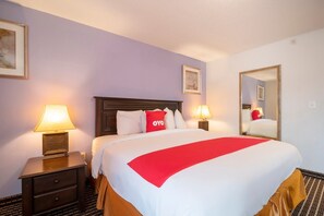A hotel room with a large bed, two bedside lamps, a nightstand with a drawer, a mirror, and a framed picture on the wall. - King Bed Non-Smoking (Houston)
