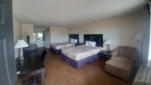 A hotel room with two beds, a desk, a chair, and a small kitchenette.