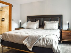 Een opgemaakt bed met een donkere hoofdbord, twee nachtkastjes met lampen, en een houten deur.