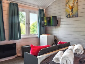Ein Zimmer mit einem Bett, einem Fernseher, einem Fenster mit Vorhängen, einem Gemälde und einem kleinen Kühlschrank.