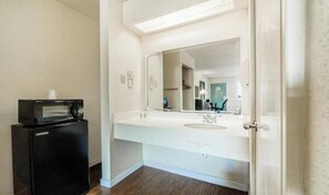 A hotel bathroom with a white sink, a mirror, and a microwave on a small cabinet.