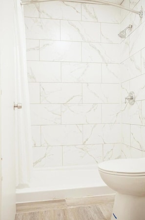 A bathroom with white marble tiles, a bathtub, and a toilet. - 2 Full Bed|Smoking|Greensboro (Greensboro)