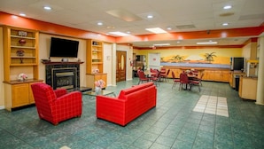 A hotel lobby with a fireplace, red sofas, a dining area, and a kitchen.