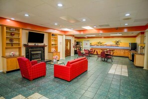 A hotel lobby with a fireplace, red sofas, a dining area, and a kitchen.