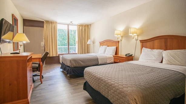 A hotel room with two beds, a desk, a chair, a dresser, and a balcony with curtains.