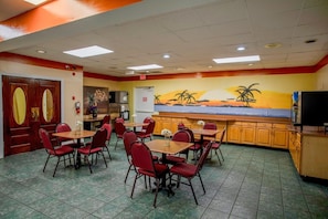 A dining area with tables and chairs, a kitchen area, and a mural on the wall. - King Bed|Non-Smoking (Greensboro)