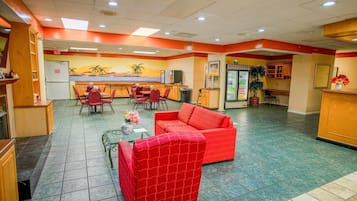 A hotel lobby with a red sofa, dining area, and a kitchen counter.