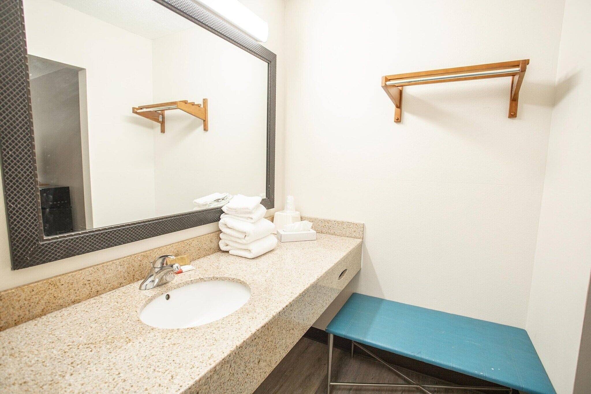 A bathroom with a sink, mirror, towel rack, and a blue bench.