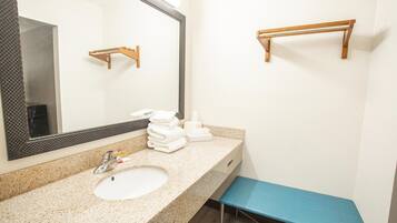 A bathroom with a sink, mirror, towel rack, and a blue bench.