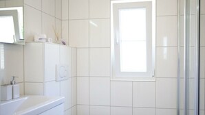 Un baño con azulejos blancos, un inodoro, un lavabo con espejo y una ventana.
