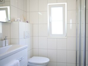 A bathroom with white tiles, a toilet, a sink with a mirror, and a window. - Holiday Home in Velsen-zuid With Terrace (Velsen-Zuid)