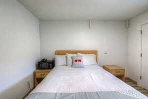 Ein Einzelbett mit Holz-Kopfteil, ein Nachttisch mit Lampe und eine kleine Kommode.