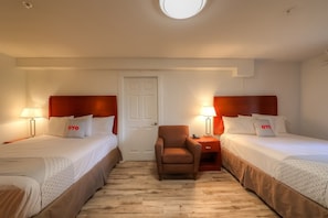 Quarto de hotel com duas camas, uma cadeira, uma mesa e uma porta.