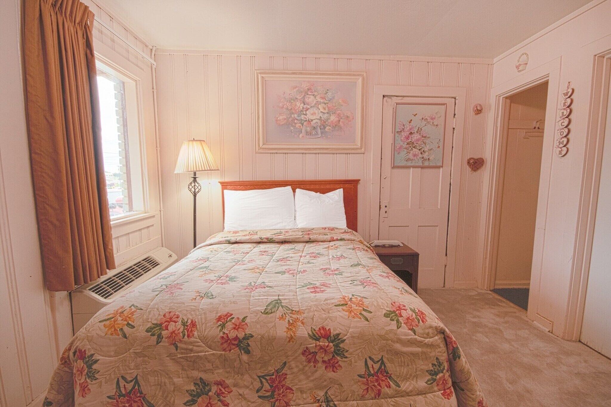 Una camera da letto con un letto, un comodino, una lampada, una finestra con tende e una porta decorata con un cuore.