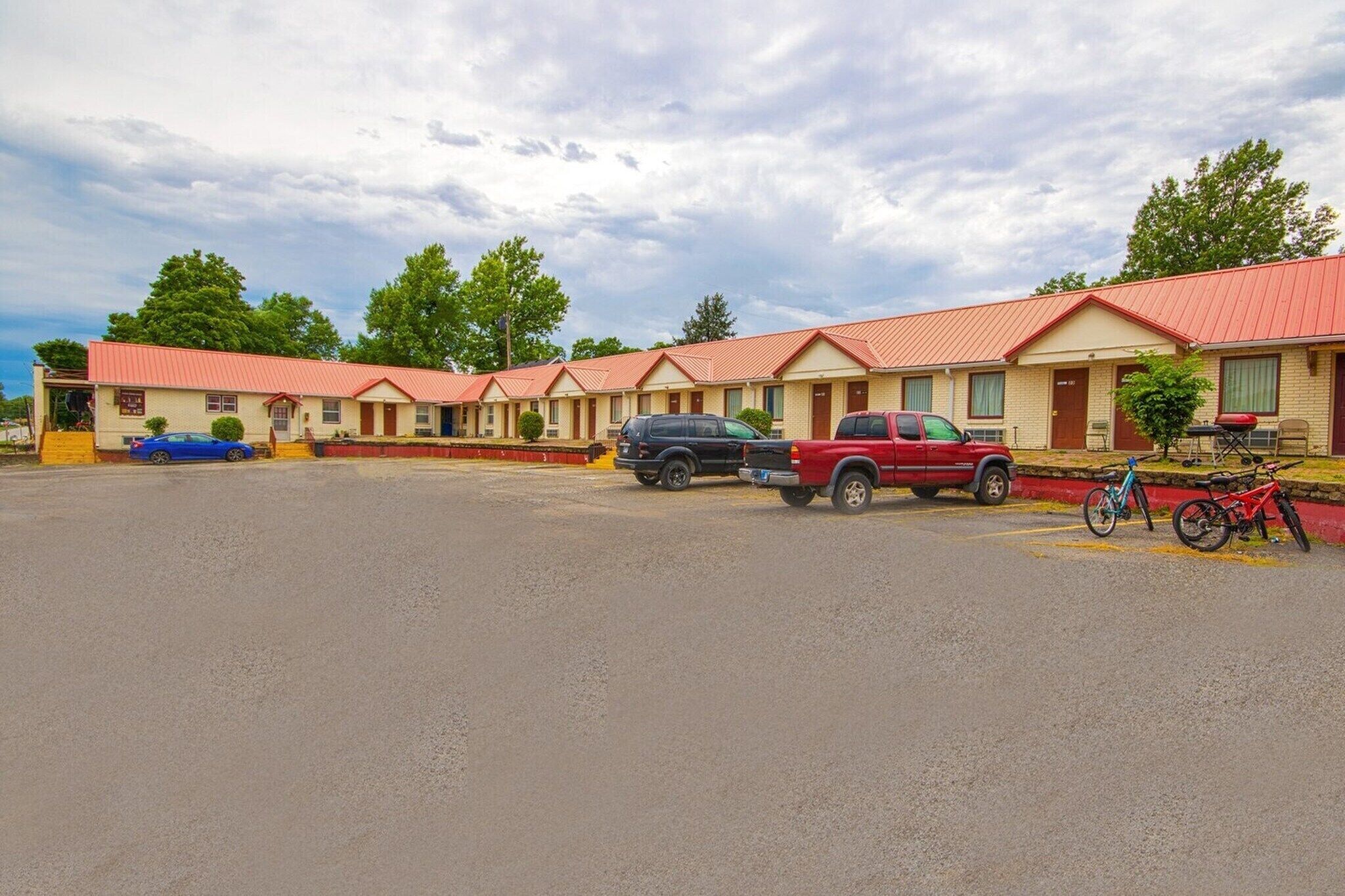A motel with multiple rooms, a parking lot, and a few parked vehicles.