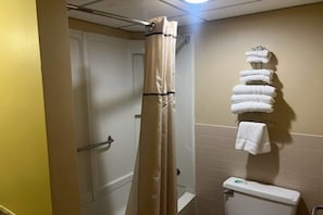 A bathroom with a shower curtain, a toilet, and a stack of towels on a rack.