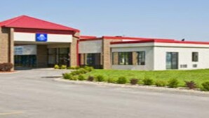 Um edifício com telhado vermelho, sinal de acessibilidade para cadeiras de rodas em azul e um estacionamento.