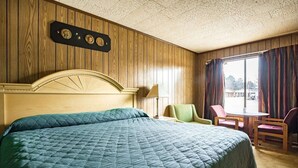 A hotel room with a large bed, a wooden headboard, a small table with chairs, and a window with curtains.