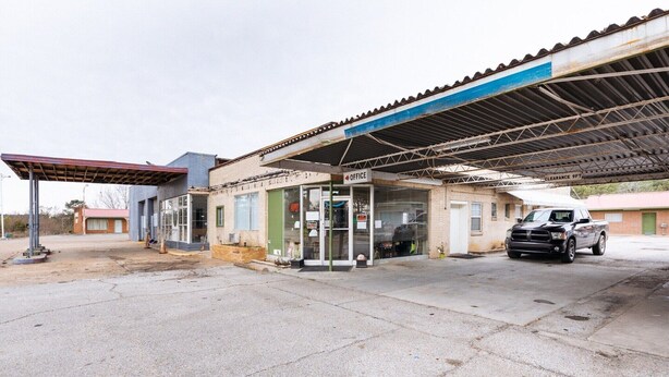 A gas station with a clear sign indicating an office, a fuel pump, and a parked vehicle.
