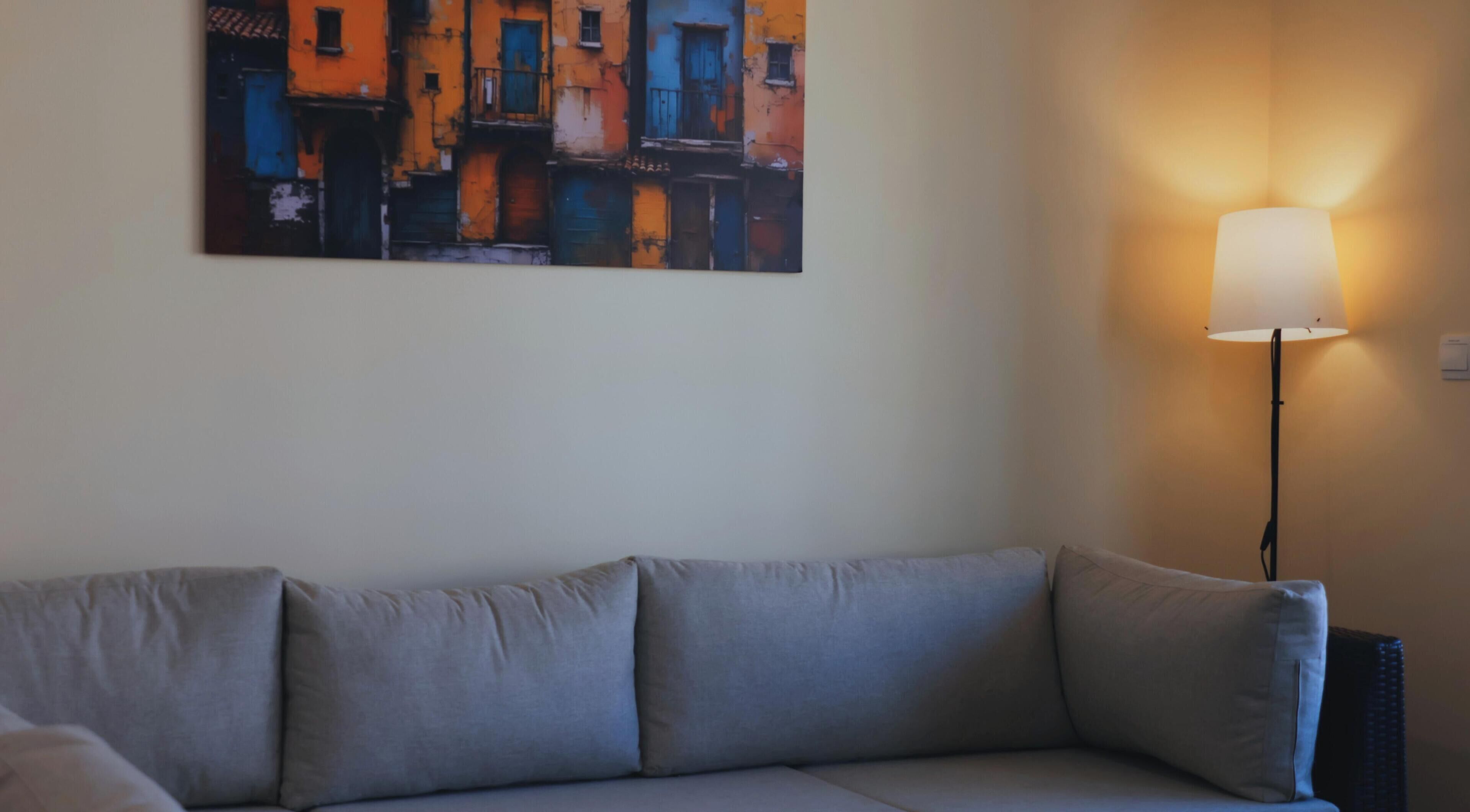 Een kamer met een grijze bank, een schilderij van gebouwen en een vloerlamp.