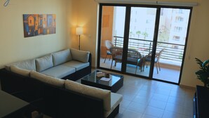 Un salon avec un canapé, une table basse et un balcon équipé de chaises.