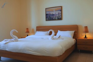 A neatly made bed with white linens, two wall-mounted lamps, and a painting on the wall.