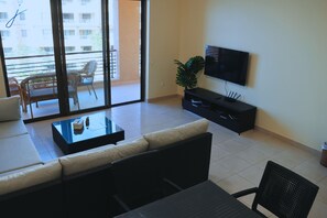 Un salón con sofá, una mesa de centro, televisor y una puerta corrediza de vidrio que da a un balcón.