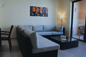 A modern living room with a grey sofa, a glass coffee table, and a painting on the wall.
