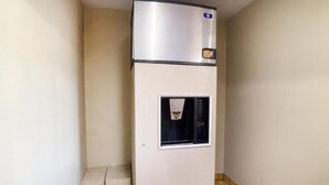 Un refrigerador compacto con compartimento congelador, ubicado en un rincón de una habitación con paredes lisas y piso de baldosas.