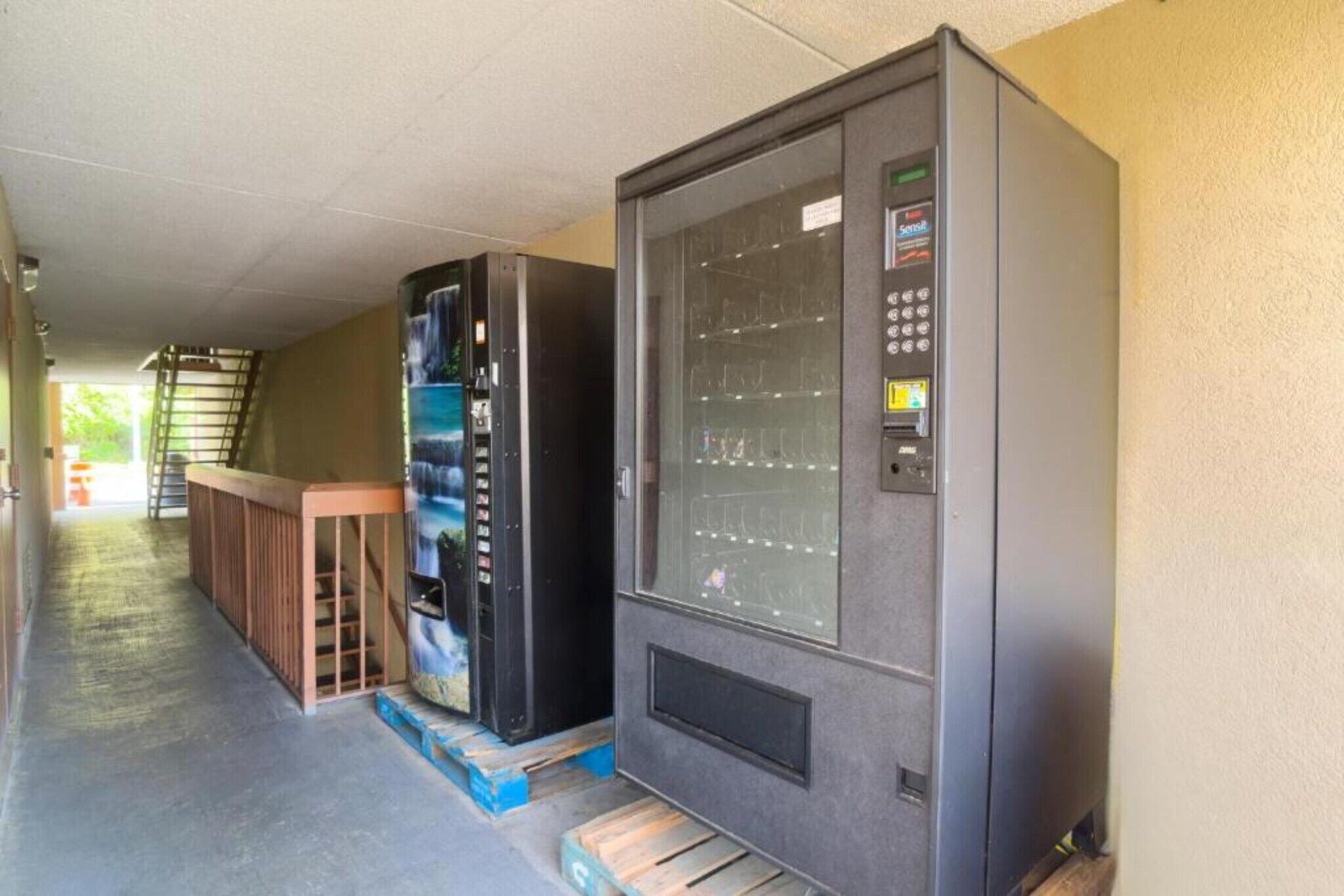 Una máquina expendedora y un refrigerador en un espacio al aire libre techado.