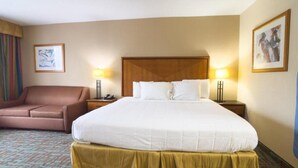 Una habitación de hotel con una cama grande, dos mesitas de noche, una silla y dos lámparas de pared.