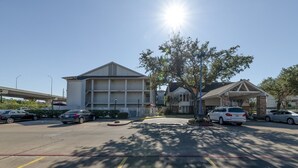 A parking lot with several cars, a building with a flat roof, and a tree casting shadows. - King Bed | Non Smoking (Houston)