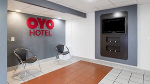 Een hotel receptie met een 'OYO HOTEL' bord, twee stoelen, een flatscreen televisie en een betegelde vloer.
