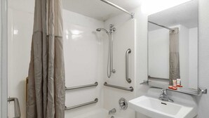 Een badkamer met een bad, wastafel, spiegel en handgrepen.