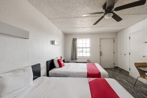 Une chambre d’hôtel avec deux lits, un ventilateur de plafond, une fenêtre avec des rideaux, une porte et une chaise.