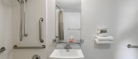 A bathroom with a white sink, a mirror, a shower with grab bars, and a towel rack.
