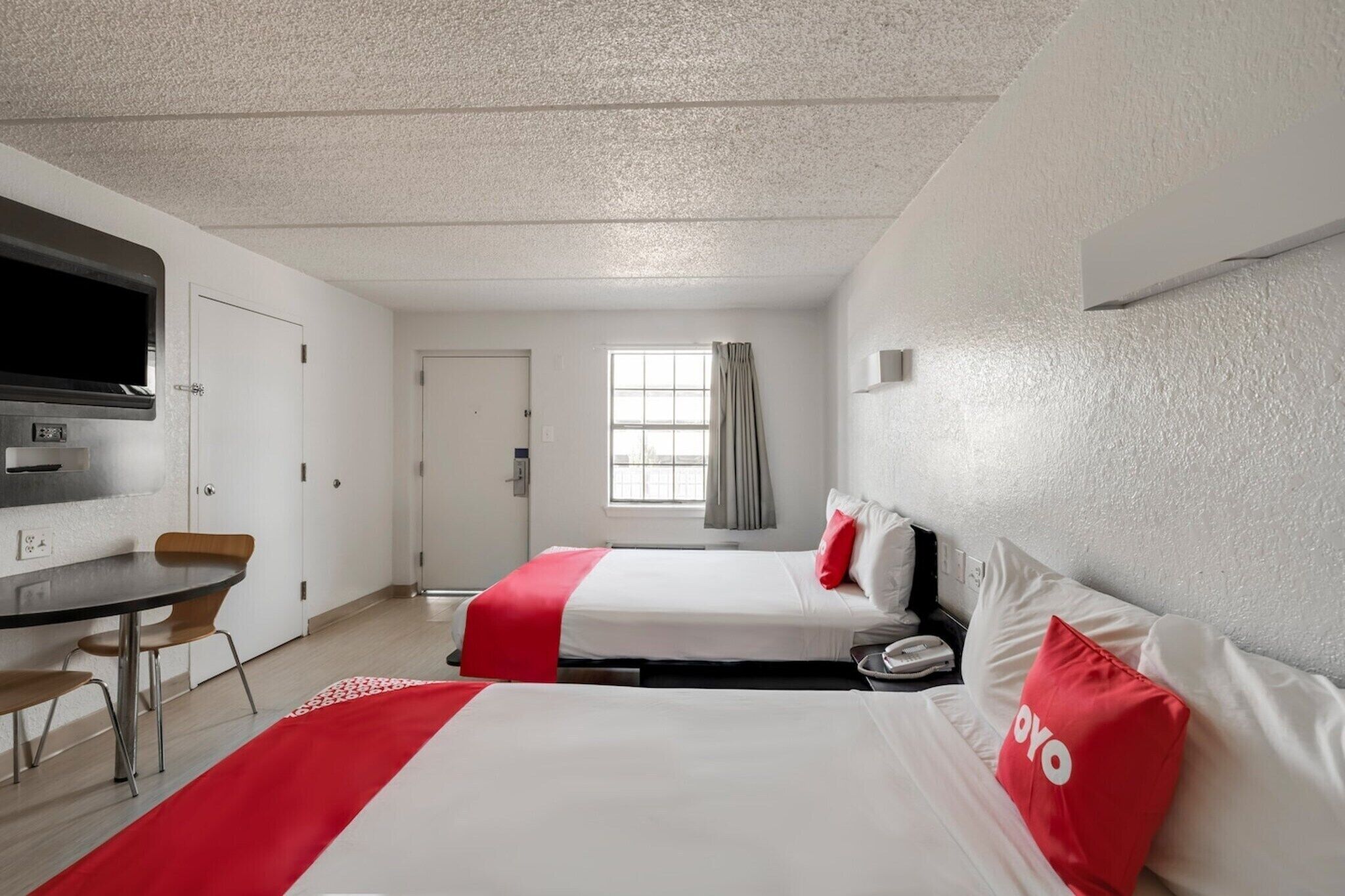 Une chambre d’hôtel avec deux lits, un bureau, une télévision et une fenêtre avec des rideaux.