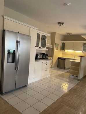 Eine moderne Küche mit einem Edelstahlkühlschrank, weißen Schränken und einem Fliesenboden.