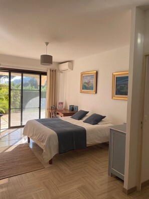 Ein Schlafzimmer mit einem Bett, einem Schreibtisch, einem Stuhl, einer kleinen Kommode und einem großen Fenster.