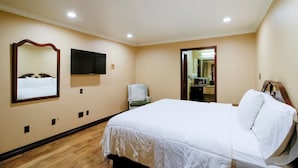 A hotel room with a bed, a chair, a TV, and a mirror on the wall. - OYO Pinewood Inn & Suites Silsbee|King Bed (Houston)