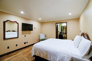A hotel room with a bed, a chair, a TV, and a mirror on the wall. - OYO Pinewood Inn & Suites Silsbee|King Bed (Houston)