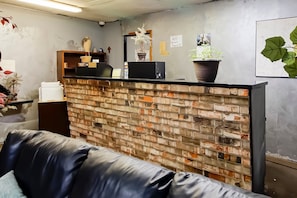 A reception desk with a brick wall, a black leather couch, and a potted plant. - OYO Pinewood Inn & Suites Silsbee|King Bed (Houston)