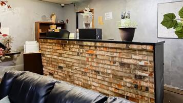A reception desk with a brick wall, a black leather couch, and a potted plant.
