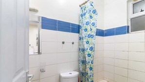 A bathroom with white tiles, a toilet, a shower curtain, and a mirror. - Cozy Studio apartment with AC in tranquil Nairobi (Nairobi)