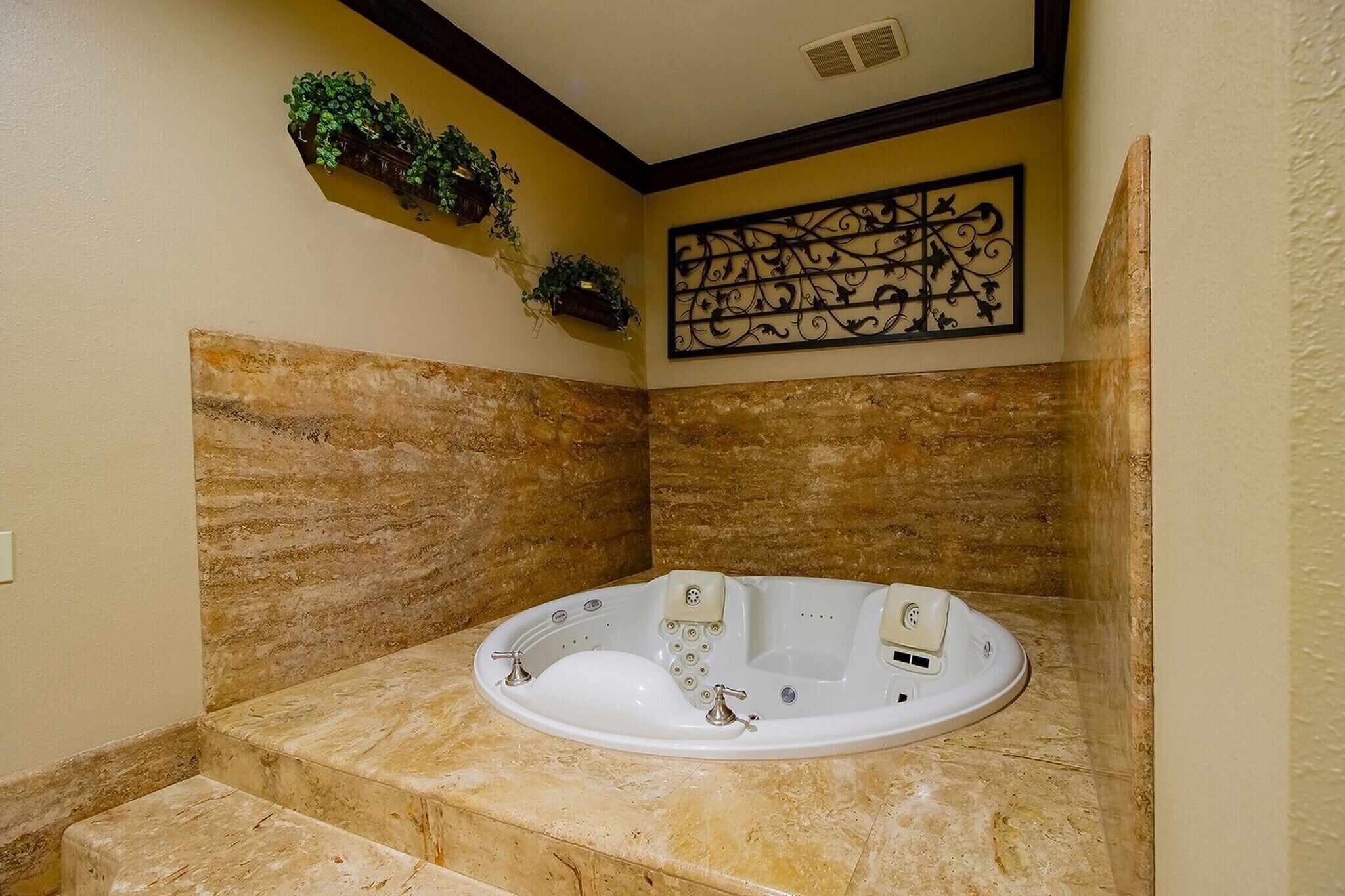 A bathroom with a freestanding bathtub, marble walls, a decorative wall piece, and a small shelf with plants.