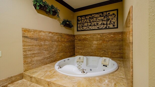Um banheiro com banheira de imersão, paredes de mármore, um objeto decorativo na parede e uma pequena estante com plantas.