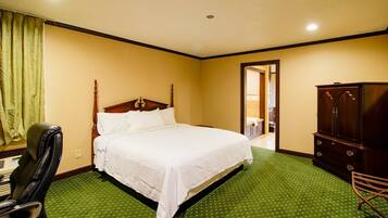A hotel room with a bed, a wooden wardrobe, a green carpet, and a chair.
